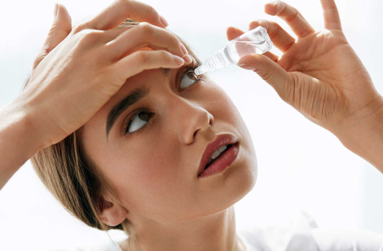 young woman carefully applying eye drops on white background