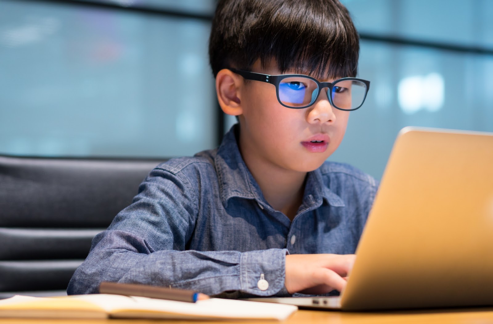 Young boy wearing blue light glasses while using laptop to finish homework