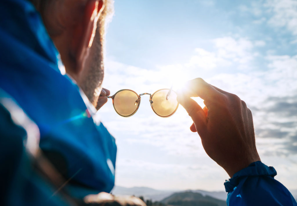 a man looks over a mountain range while hold up a pair of polarized sunglasses