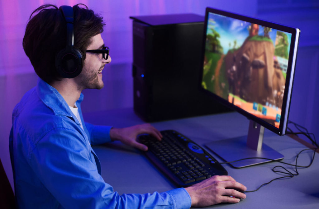 A man wears blue light glasses while playing video games on a computer at arm's length from his eyes to reduce eye strain
