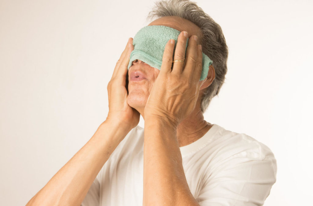 A man applies a warm compress to both eyes to relieve eye discomfort.