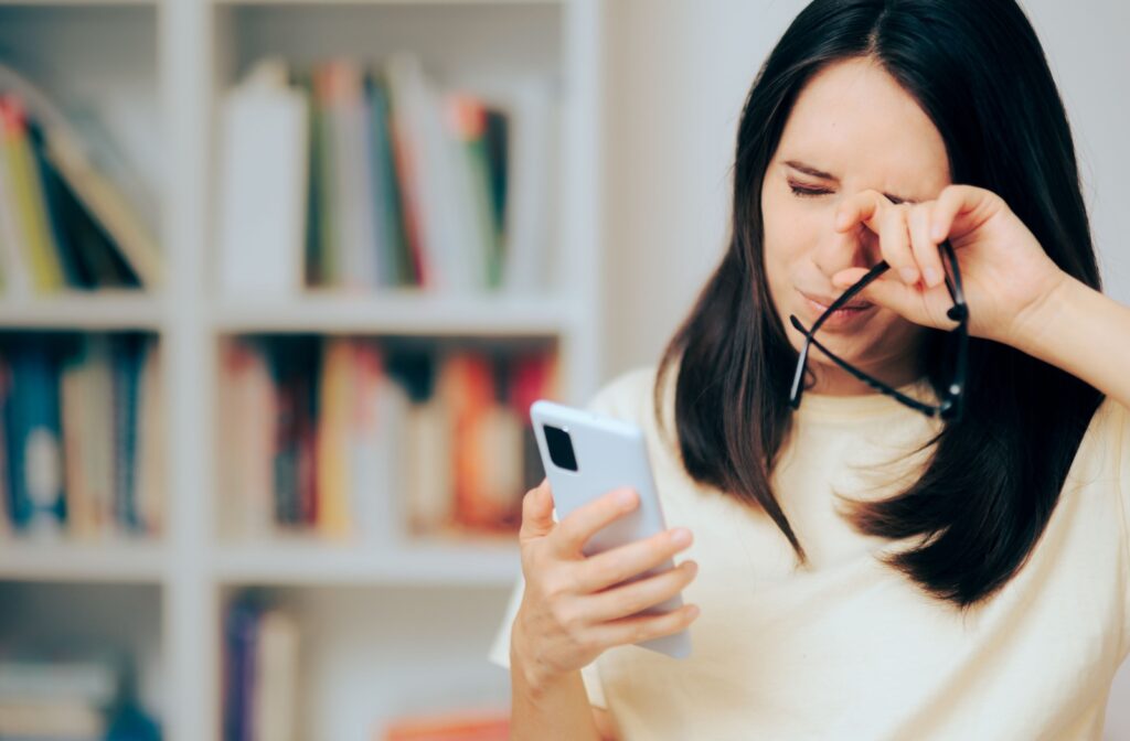 A woman holding her phone and rubbing her left eye.