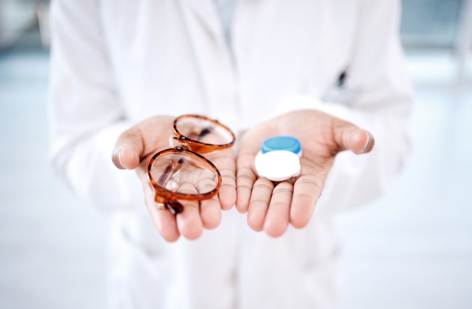 A close up of an eye doctor's hands holding a contact lens case in one and eyeglasses in the other.